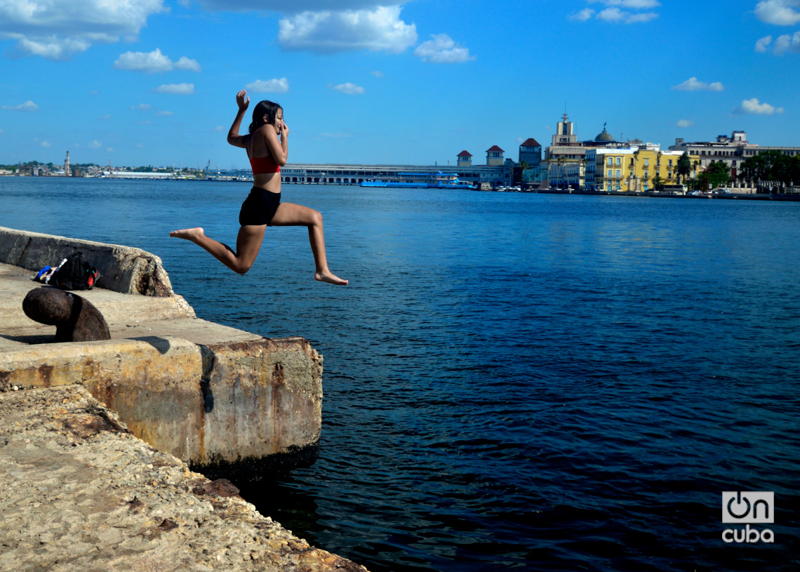 Una joven se lanza al mar desde el antiguo Muelle del Carbón, en Casablanca. Detrás, una vista de La Habana. Foto: Otmaro Rodríguez.
