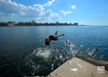 Un joven se lanza al mar haciendo piruetas desde el antiguo Muelle del Carbón, en Casablanca. En la distancia, La Habana. Foto: Otmaro Rodríguez.