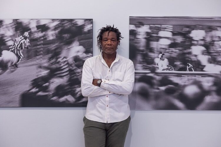 El artista Carlos Torres Cairo flanqueado por fotos suyas que capturan el vértigo del Palio. Foto: Cortesía de Aurelia Ediciones