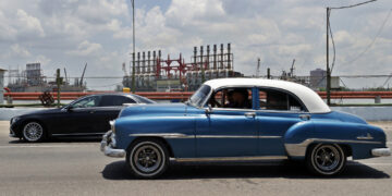 Autos transitan frente a las patanas turcas, generadoras de electricidad, desde la bahía de La Habana. Foto:  Ernesto Mastrascusa/EFE.