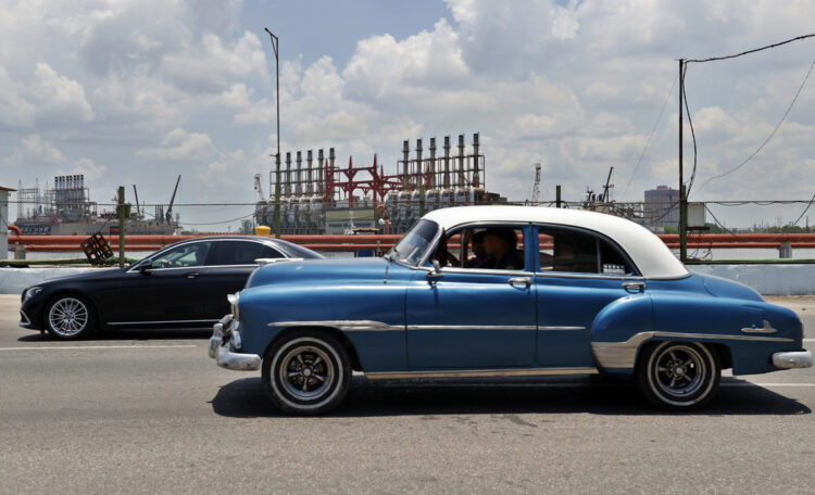 Autos transitan frente a las patanas turcas, generadoras de electricidad, desde la bahía de La Habana. Foto:  Ernesto Mastrascusa/EFE.