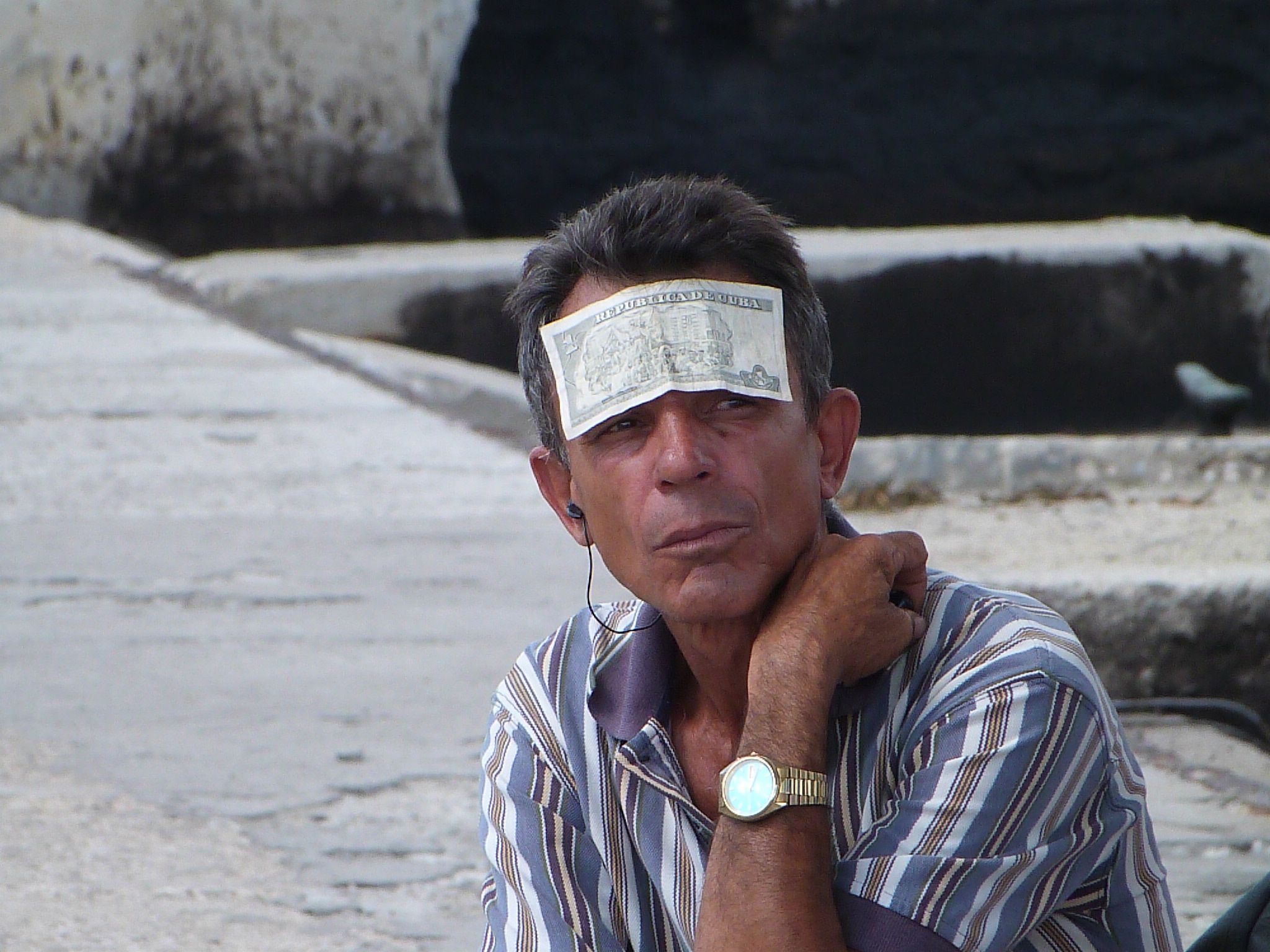 Un hombre se cubre la frente del sol con un billete de un peso cubano, una cuantía monetaria totalmente en desuso ante la elevada inflación en la isla. Foto: AMD.