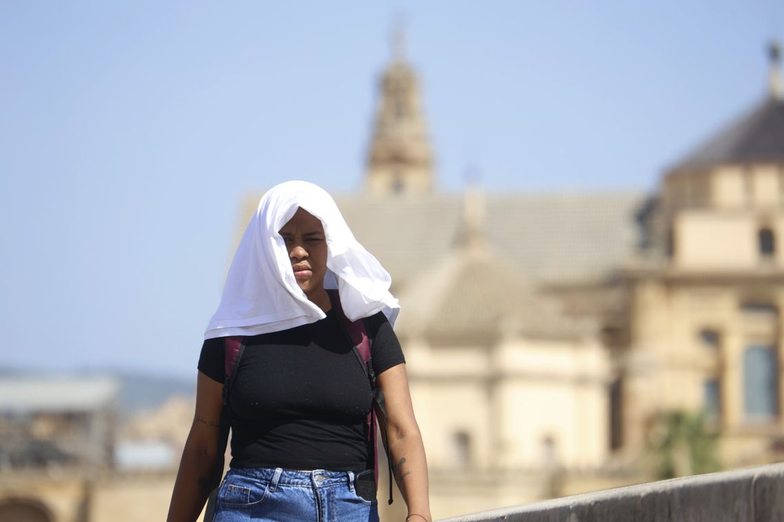 Una mujer se tapa con una camiseta para protegerse del calor, mientras camina por el Puente Romano, en Córdoba, España. Foto: Salas / EFE.