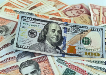 Un billete de 100 dólares junto a billetes de varias denominaciones de pesos cubanos. Foto: Ernesto Mastrascusa / EFE.