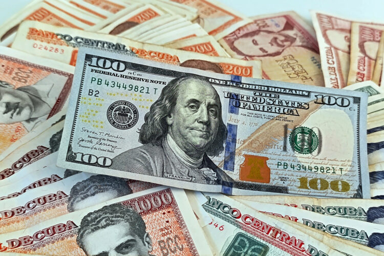 Un billete de 100 dólares junto a billetes de varias denominaciones de pesos cubanos. Foto: Ernesto Mastrascusa / EFE.