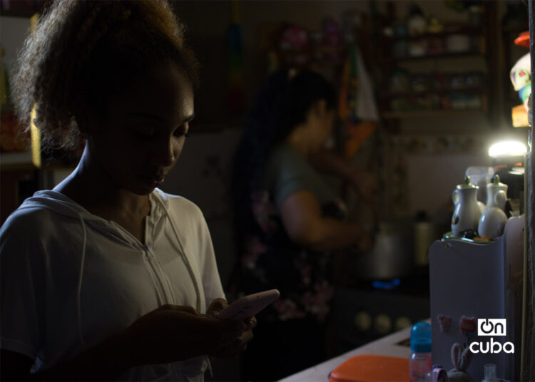 Una joven revisa su teléfono móvil durante un apagón en La Habana. Foto: Otmaro Rodríguez.
