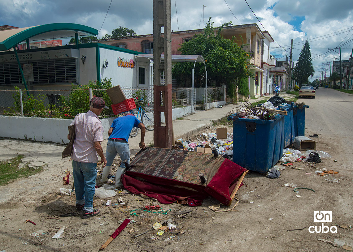 Unos hombres intentan quitarle las patas a un sofá votado en un vertedero de basura, en el reparto Sevillano. Foto: Otmaro Rodríguez.