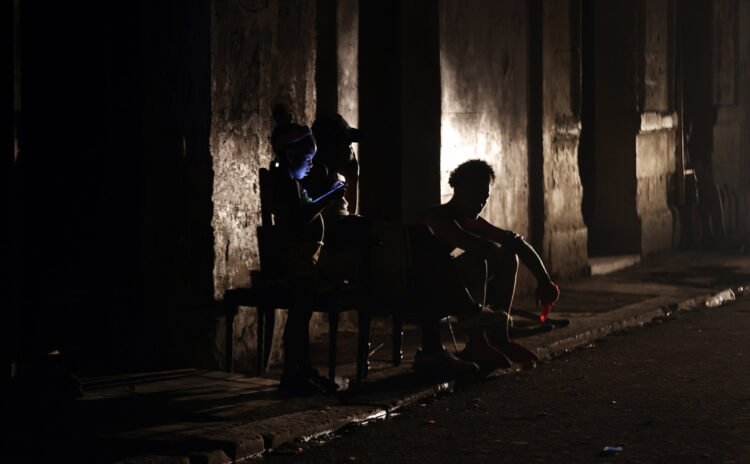 Personas sentadas en una acera esperan el regreso de la electricidad, en medio de un apagón en La Habana. Foto: Ernesto Mastrascusa / EFE.