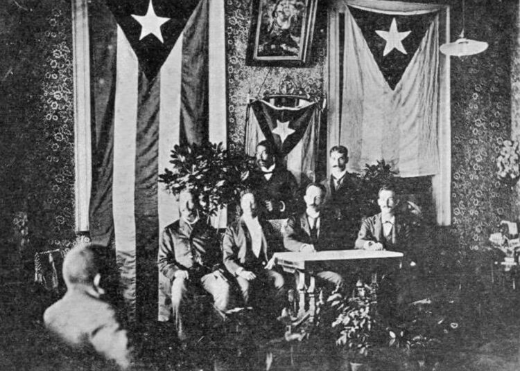 Foto tomada el 10 de octubre de 1892 en la que aparece Martí presidiendo el Cuerpo del Consejo de Kingston. Se observan desplegadas a su derecha la bandera de Cuba y a su izquierda la de Puerto Rico. Foto: Iconografía Martiana.