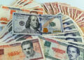 Un billete de 100 dólares junto a billetes de varias denominaciones de pesos cubanos. Foto: Ernesto Mastrascusa / EFE.