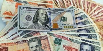 Un billete de 100 dólares junto a billetes de varias denominaciones de pesos cubanos. Foto: Ernesto Mastrascusa / EFE.