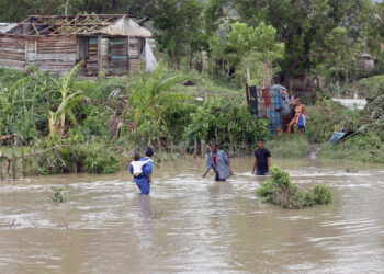 Personas cruzan un río crecido en el municipio de Guamá en Santiago de Cuba, tras el paso del potente huracán Melissa. Foto: Ernesto Mastrascusa / EFE.