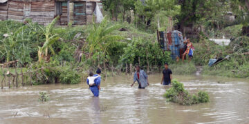 Personas cruzan un río crecido en el municipio de Guamá en Santiago de Cuba, tras el paso del potente huracán Melissa. Foto: Ernesto Mastrascusa / EFE.