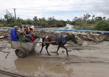 AME3289. SANTIAGO DE CUBA (CUBA), 29/10/2025.- Personas montadas en una carreta cruzan un puente cubierto de lodo este miércoles, en el poblado de Guama en Santiago de Cuba (Cuba). Melissa se aleja de Cuba convertido en un huracán de categoría 2, con vientos máximos sostenidos de hasta 160 kilómetros por hora, y comienza a dirigirse hacia las Bahamas, tras provocar inundaciones, crecidas de ríos y corrimientos de tierras en el este cubano. EFE/ Ernesto Mastrascusa