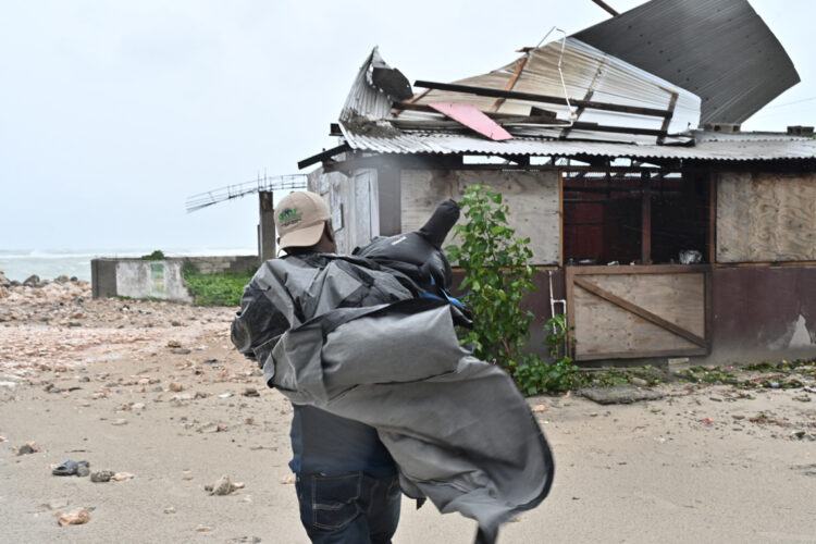 Un hombre carga una lona para cubrir el techo de una casa antes del paso del huracán Melissa, en la playa pesquera de Hellshire, en Portmore, Jamaica. Foto: Rudolph Brown/EFE.