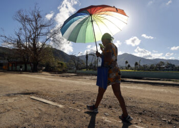 En el pueblo de El Cobre, en Santiago de Cuba, severamente golpeado por el huracán Melissa, una mujer camina protegiéndose del intenso sol. Foto: EFE/ Ernesto Mastrascusa.