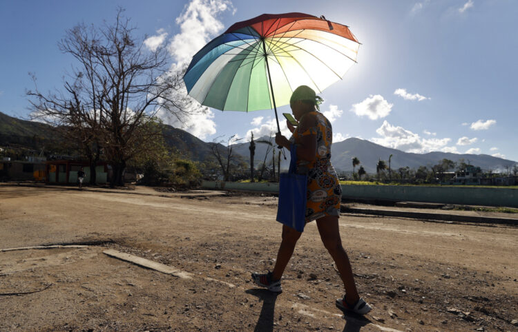 En el pueblo de El Cobre, en Santiago de Cuba, severamente golpeado por el huracán Melissa, una mujer camina protegiéndose del intenso sol. Foto: EFE/ Ernesto Mastrascusa.