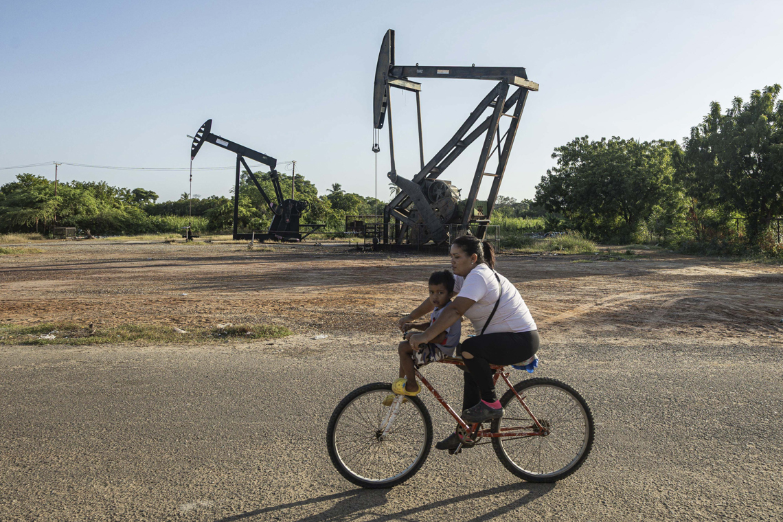 Una mujer conduce junto a un niño una bicicleta frente a balancines petroleros en Cabimas, Venezuela, país que posee las reservas probadas más grandes del mundo. Foto: Henry Chirinos / EFE,