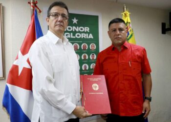 El primer vicepresidente de la Asamblea Nacional de Venezuela, Pedro Infante, (der) entrega al embajador de Cuba, Jorge Luis Mayo, un acuerdo que declara “héroes y mártires” a los 32 militares cubanos muertos en los ataques de EE.UU. Foto: Asamblea Nacional de Venezuela / Facebook.