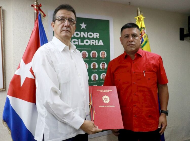 El primer vicepresidente de la Asamblea Nacional de Venezuela, Pedro Infante, (der) entrega al embajador de Cuba, Jorge Luis Mayo, un acuerdo que declara “héroes y mártires” a los 32 militares cubanos muertos en los ataques de EE.UU. Foto: Asamblea Nacional de Venezuela / Facebook.
