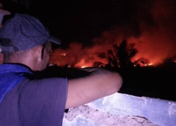 Un hombre observa desde un balcón el incendio desatado en torno al reparto Armando Mestre, en la zona conocida como El Naranjal, en Matanzas, en la noche del 13 de enero de 2026. Foto: Periódico Girón / Facebook.