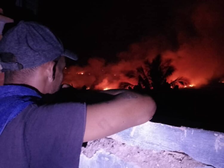 Un hombre observa desde un balcón el incendio desatado en torno al reparto Armando Mestre, en la zona conocida como El Naranjal, en Matanzas, en la noche del 13 de enero de 2026. Foto: Periódico Girón / Facebook.