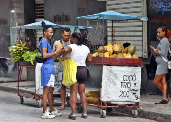 Mujeres y hombres en los alrededores de un puesto de venta callejera de coco, en una calle de La Habana. Foto: Ernesto Mastrascusa / EFE.