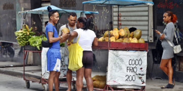 Mujeres y hombres en los alrededores de un puesto de venta callejera de coco, en una calle de La Habana. Foto: Ernesto Mastrascusa / EFE.