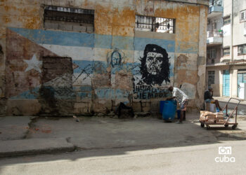 Un hombre carga un tanque de agua frente a un mural con la bandera cubana y la imagen del Che Guevara en una calle de La Habana. Foto: Otmaro Rodríguez.