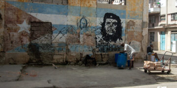 Un hombre carga un tanque de agua frente a un mural con la bandera cubana y la imagen del Che Guevara en una calle de La Habana. Foto: Otmaro Rodríguez.