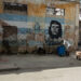 Un hombre carga un tanque de agua frente a un mural con la bandera cubana y la imagen del Che Guevara en una calle de La Habana. Foto: Otmaro Rodríguez.