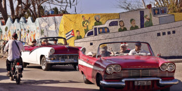 Turistas pasean en autos clásicos frente a un mural del artista plástico Fuster, en Jaimanitas, La Habana. Foto: Ernesto Mastrascusa / EFE.