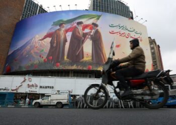 Un hombre en una moto pasa frente a un enorme cartel publicitario que muestra a los difuntos líderes supremos iraníes, el ayatolá Ruhollah Jomeini, el ayatolá Ali Jamenei , y al nuevo líder supremo iraní, el ayatolá Mojtaba Jamenei (d), en la Plaza Valiasr de Teherán. Foto: Abedin Taherkenareh / EFE.