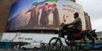 Un hombre en una moto pasa frente a un enorme cartel publicitario que muestra a los difuntos líderes supremos iraníes, el ayatolá Ruhollah Jomeini, el ayatolá Ali Jamenei , y al nuevo líder supremo iraní, el ayatolá Mojtaba Jamenei (d), en la Plaza Valiasr de Teherán. Foto: Abedin Taherkenareh / EFE.
