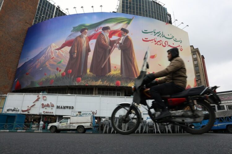 Un hombre en una moto pasa frente a un enorme cartel publicitario que muestra a los difuntos líderes supremos iraníes, el ayatolá Ruhollah Jomeini, el ayatolá Ali Jamenei , y al nuevo líder supremo iraní, el ayatolá Mojtaba Jamenei (d), en la Plaza Valiasr de Teherán. Foto: Abedin Taherkenareh / EFE.