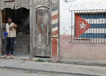 Un hombre en la entrada de un antiguo edificio, con un ventana enrejada con la bandera de Cuba, en La Habana. Foto: Ernesto Mastrascusa / EFE / Archivo.