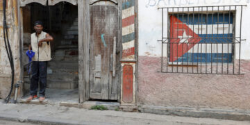 Un hombre en la entrada de un antiguo edificio, con un ventana enrejada con la bandera de Cuba, en La Habana. Foto: Ernesto Mastrascusa / EFE / Archivo.