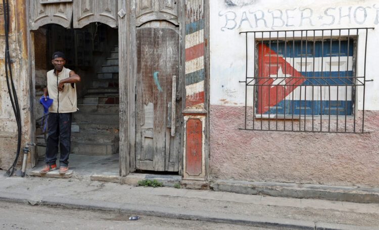 Un hombre en la entrada de un antiguo edificio, con un ventana enrejada con la bandera de Cuba, en La Habana. Foto: Ernesto Mastrascusa / EFE / Archivo.