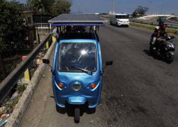 Triciclo eléctrico con un panel instalado transitando una vía habanera. Foto: EFE/STR