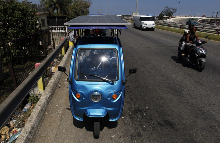 Triciclo eléctrico con un panel instalado transitando una vía habanera. Foto: EFE/STR