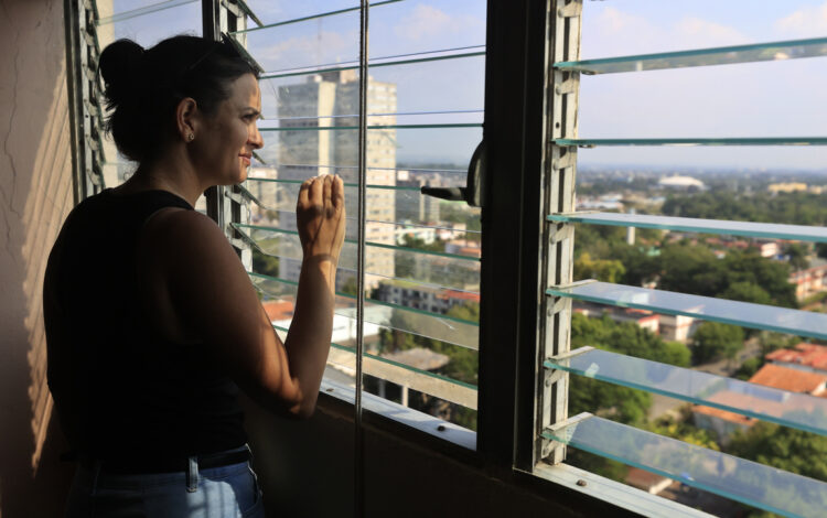 Una mujer observa la ciudad desde la ventana de su casa, en La Habana. Foto: Ernesto Mastrascusa/EFE.