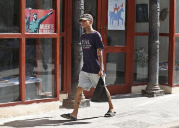 Un joven con una camiseta de EE.UU camina junto a un cartel alegórico a la Revolución Cubana, en La Habana. Foto: Ernesto Mastrascusa / EFE.