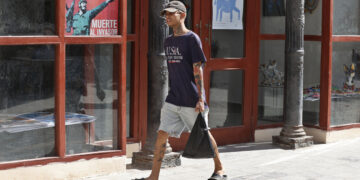Un joven con una camiseta de EE.UU camina junto a un cartel alegórico a la Revolución Cubana, en La Habana. Foto: Ernesto Mastrascusa / EFE.