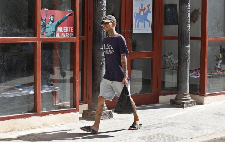 Un joven con una camiseta de EE.UU camina junto a un cartel alegórico a la Revolución Cubana, en La Habana. Foto: Ernesto Mastrascusa / EFE.