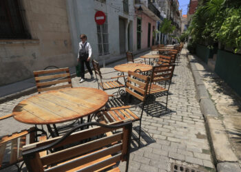 Una persona camina frente a mesas y sillas vacías en La Habana, en medio del significativo declive del turismo en Cuba en 2026. Foto: Ernesto Mastrascusa / EFE.