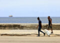 Dos hombres caminan por el Malecón de La Habana, mientras un barco se aleja de Cuba. Foto: Ernesto Mastrascusa / EFE.