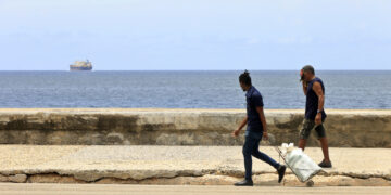 Dos hombres caminan por el Malecón de La Habana, mientras un barco se aleja de Cuba. Foto: Ernesto Mastrascusa / EFE.