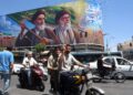 Un iraní hace el signo de la victoria mientras pasa en coche junto a una valla publicitaria de los difuntos líderes supremos iraníes, el ayatolá Ruhollah Khomeini y el ayatolá Ali Khamenei, en una calle de Teherán, Irán, el 15 de junio de 2026. Foto: EFE/EPA/ABEDIN TAHERKENAREH.