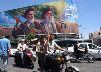 Un iraní hace el signo de la victoria mientras pasa en coche junto a una valla publicitaria de los difuntos líderes supremos iraníes, el ayatolá Ruhollah Khomeini y el ayatolá Ali Khamenei, en una calle de Teherán, Irán, el 15 de junio de 2026. Foto: EFE/EPA/ABEDIN TAHERKENAREH.