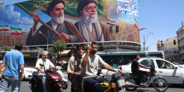 Un iraní hace el signo de la victoria mientras pasa en coche junto a una valla publicitaria de los difuntos líderes supremos iraníes, el ayatolá Ruhollah Khomeini y el ayatolá Ali Khamenei, en una calle de Teherán, Irán, el 15 de junio de 2026. Foto: EFE/EPA/ABEDIN TAHERKENAREH.